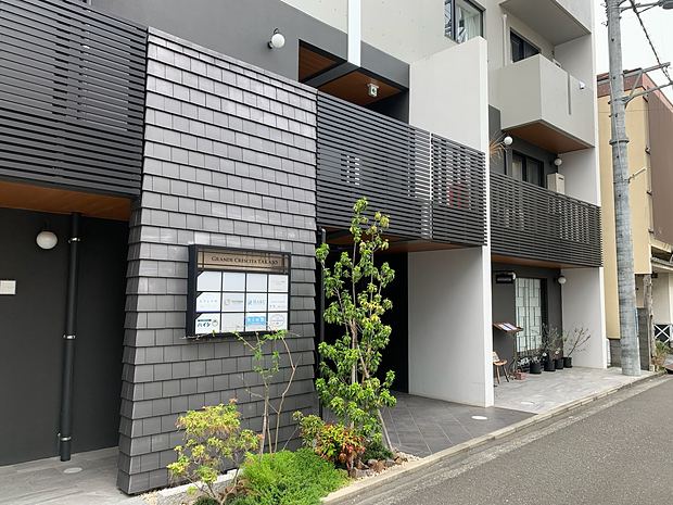 We are on the ground floor (1F) of the gray and black apartment building, in the unit just past the electronic signboard