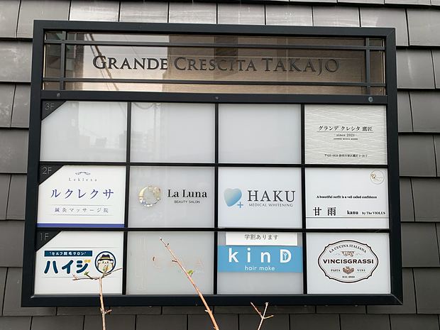 We are on the ground floor (1F) of the gray and black apartment building, in the unit just past the electronic signboard