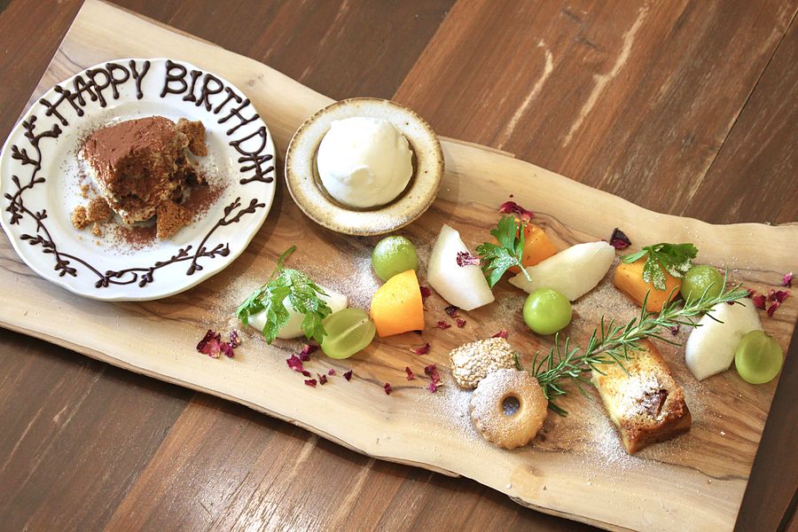 誕生日プレート。チョコレートで HAPPY BIRTHDAY と書いたお皿と、ドルチェ・フルーツ・焼き菓子を盛り合わせた木の板